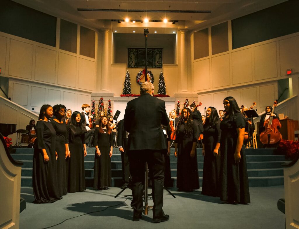 Choir in black attire sings at a church with Christmas decorations.