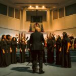 Choir in black attire sings at a church with Christmas decorations.
