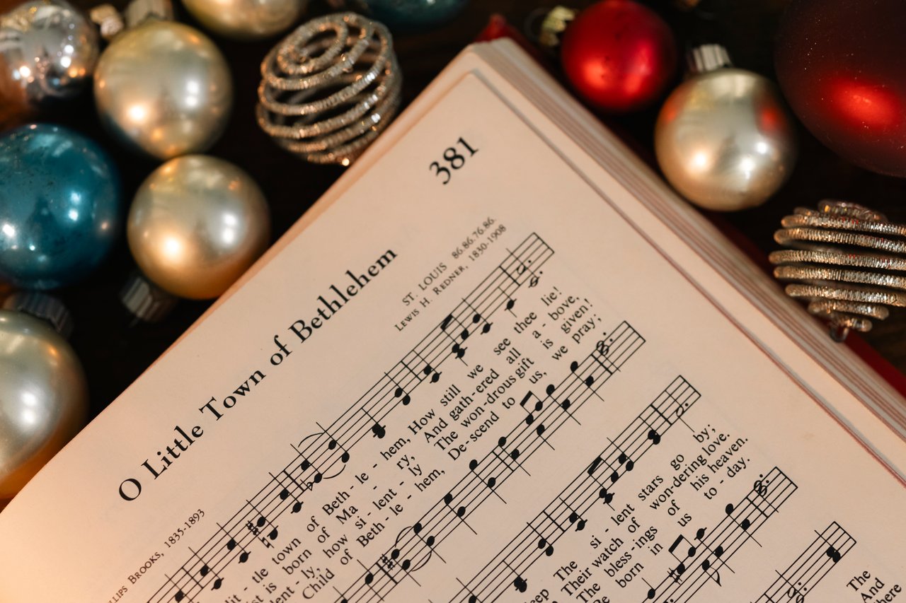 gallery-2 Open hymnbook displaying 'O Little Town of Bethlehem' surrounded by festive holiday baubles.