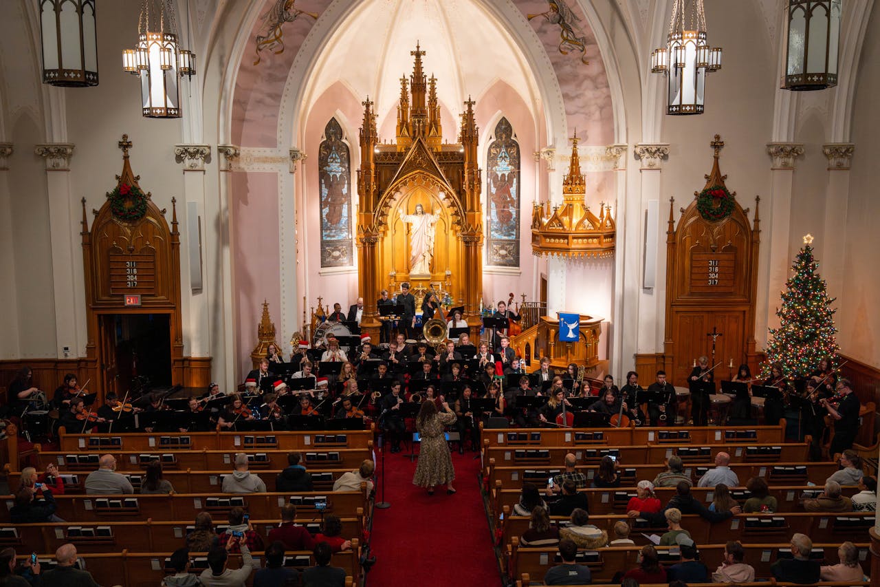 An orchestra performing a Christmas concert in a grand church with seasonal decorations.
