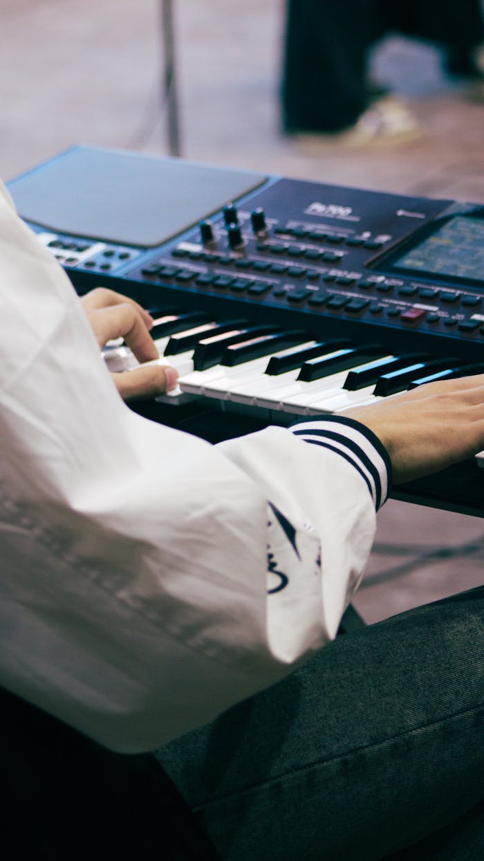 gallery-6 A musician wearing a white shirt plays an electronic keyboard indoors during the day.