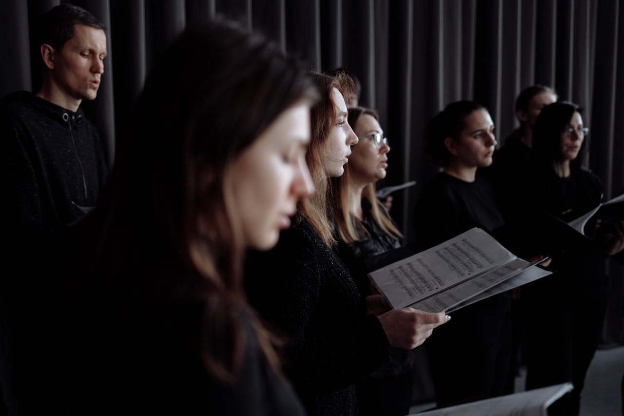 services-02 Adult choir practicing in an indoor studio performance setting with music sheets.
