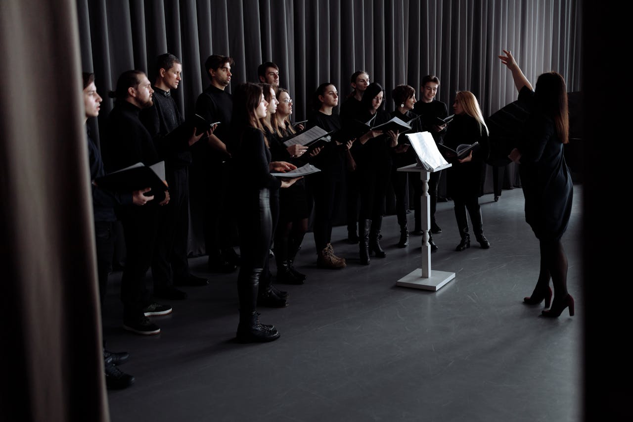 hero-img-01 A choir practicing under a conductor's guidance in an indoor studio setting.