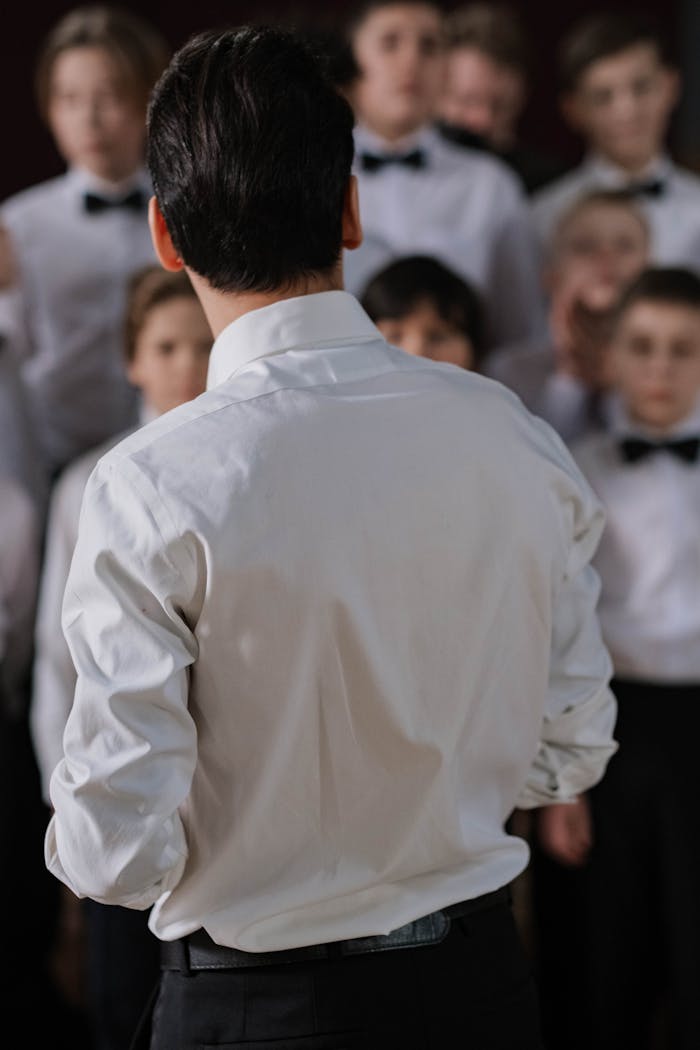 about-01 Back view of a choir director guiding children in a musical performance.
